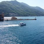 Drone view of a Good Hope Tours speed boat near Our Lady of the Rocks island, with mountains in the background and the sea surrounding them.